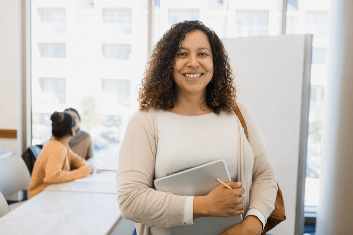 Unlock your potential with Employable Me Young Latin American woman holding a laptop in a modern office, smiling confidently.